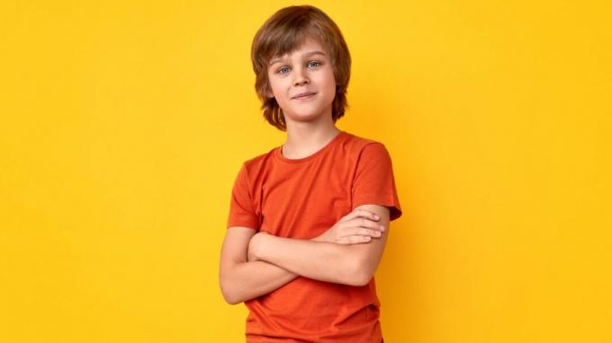Позитивни дечак претента у неформалној одећи држећи прекрижене руке и гледајући камеру на живописној жутој позадини